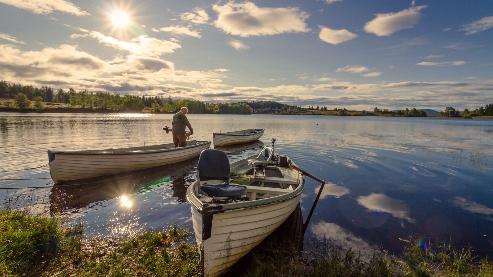Fisherman beside small wooden boats on a calm lake at sunrise